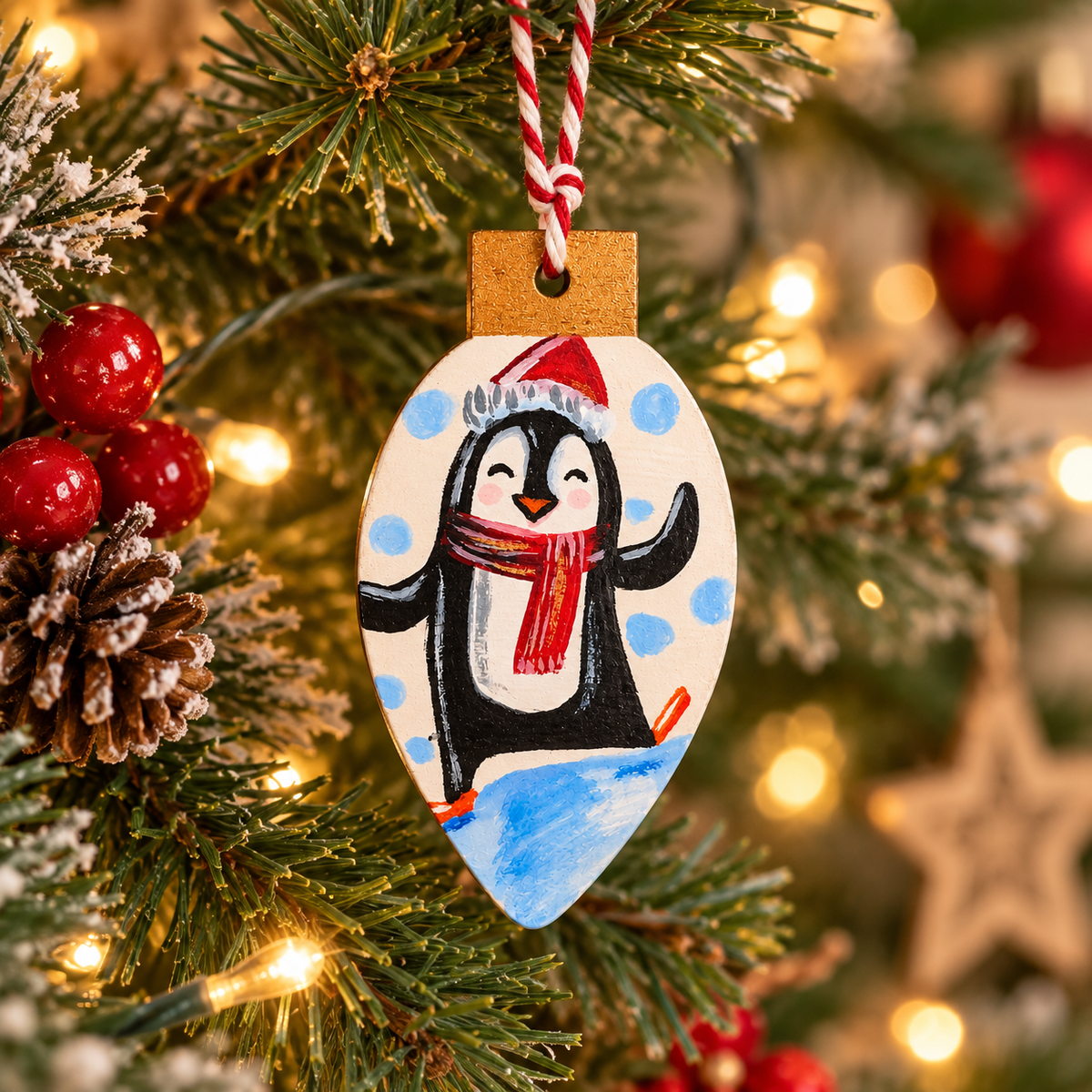 Hand-painted wooden penguin Christmas ornament hanging on a decorated Christmas tree with warm fairy lights and festive decorations