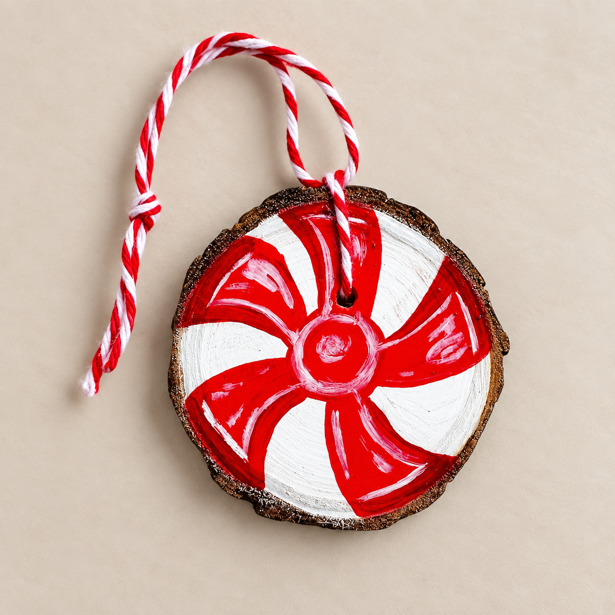 Natural wood slice hand painted with a red and white peppermint candy cane-style design and finished with twisted hanging twine.