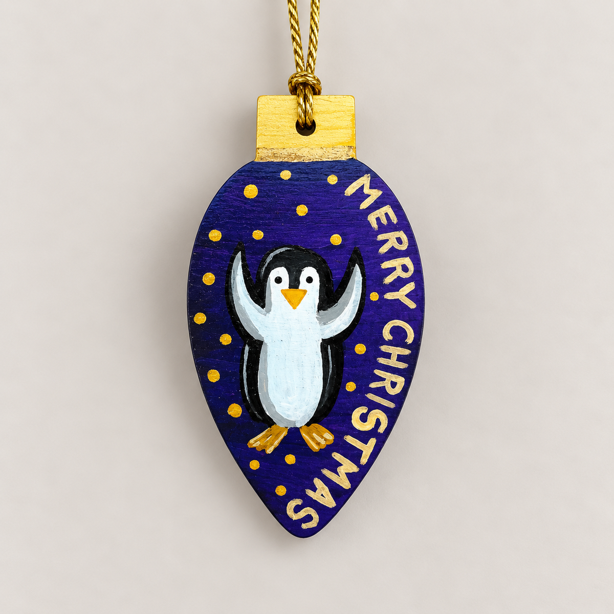 Hand-painted wooden Christmas ornament featuring a cheerful penguin on a deep blue background with gold stars and Merry Christmas lettering