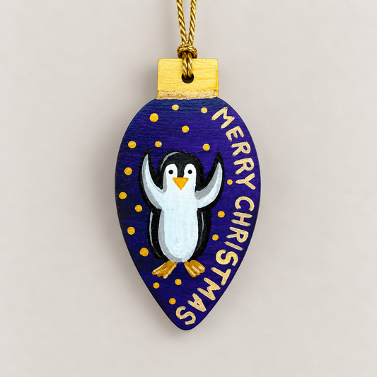 Hand-painted wooden Christmas ornament featuring a cheerful penguin on a deep blue background with gold stars and Merry Christmas lettering