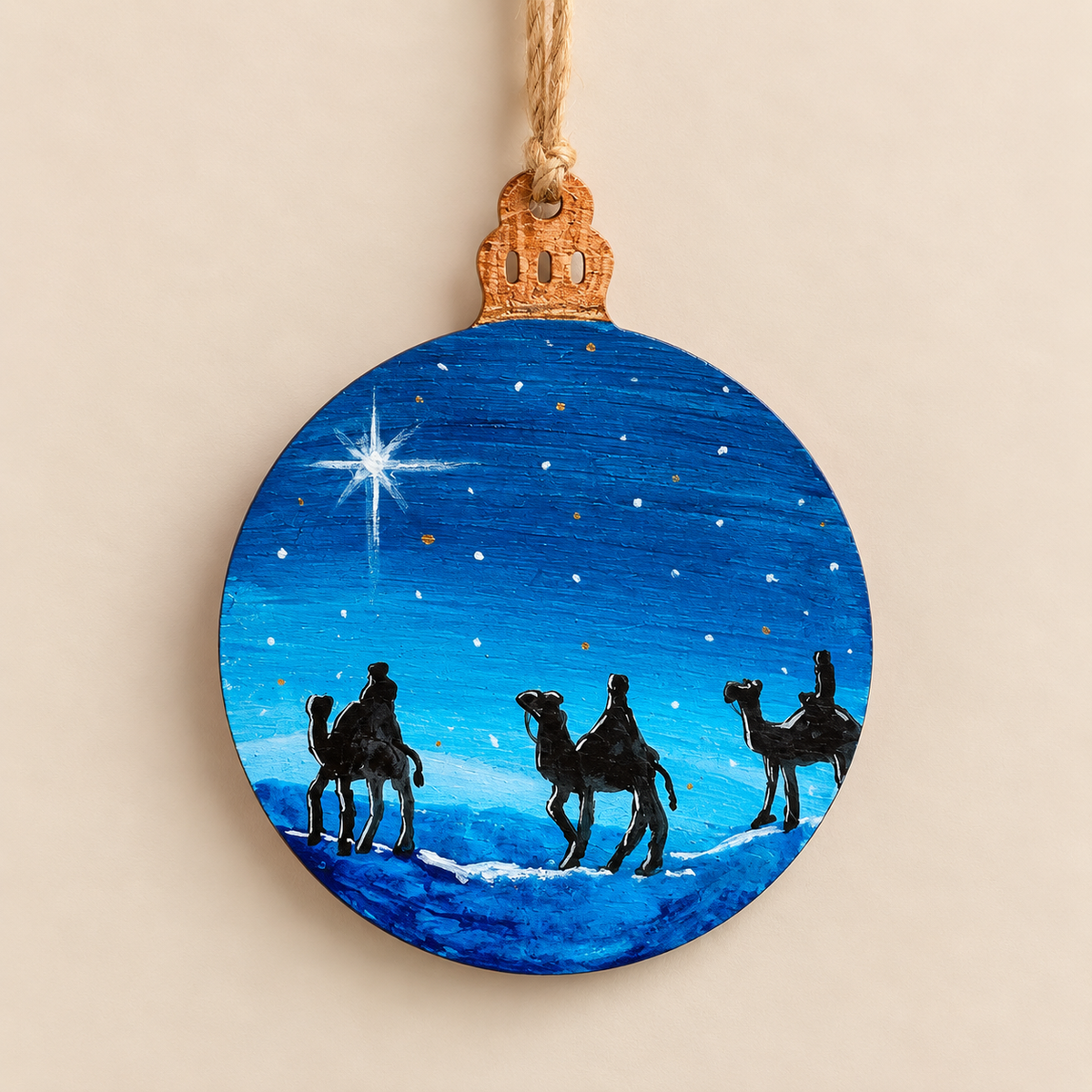 Hand painted wooden Christmas ornament showing three wise men travelling by camel beneath a starry blue night sky.
