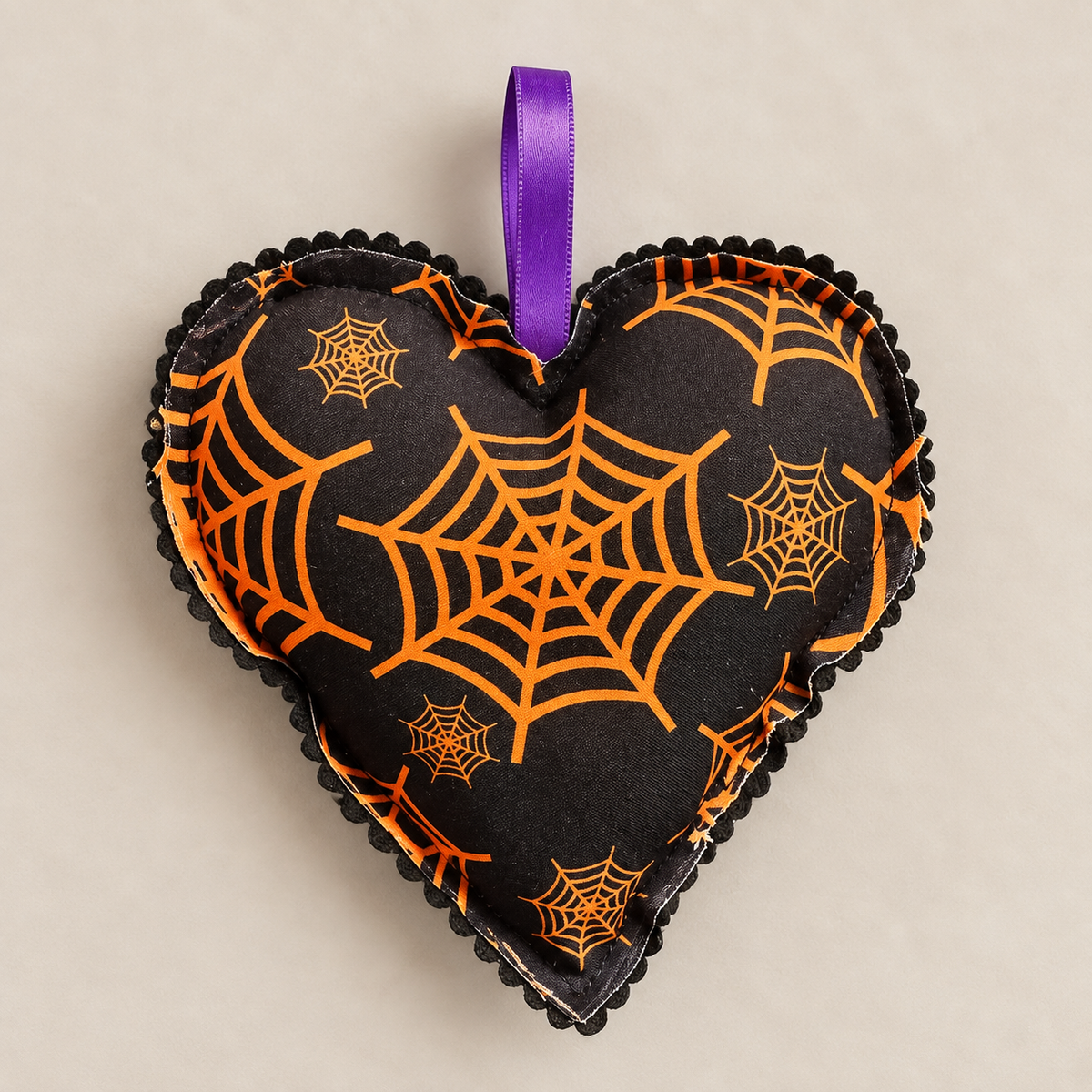 Handmade black fabric Halloween heart with orange spiderwebs, black felt backing and purple hanging loop