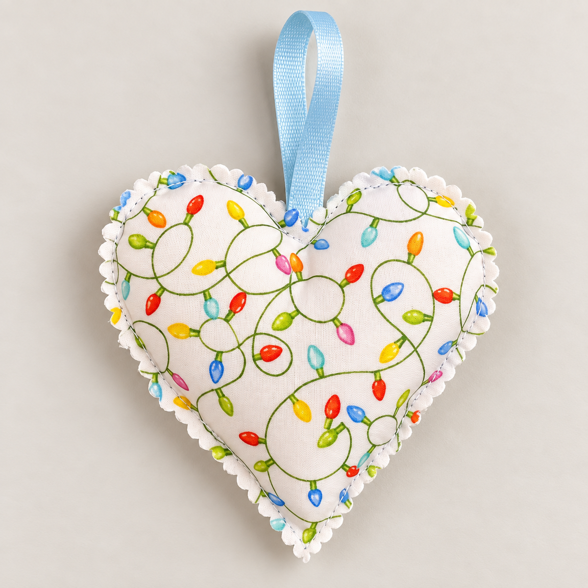 Handmade white Christmas fabric heart decorated with colourful red, green, blue and yellow Christmas lights, with a pale blue hanging ribbon