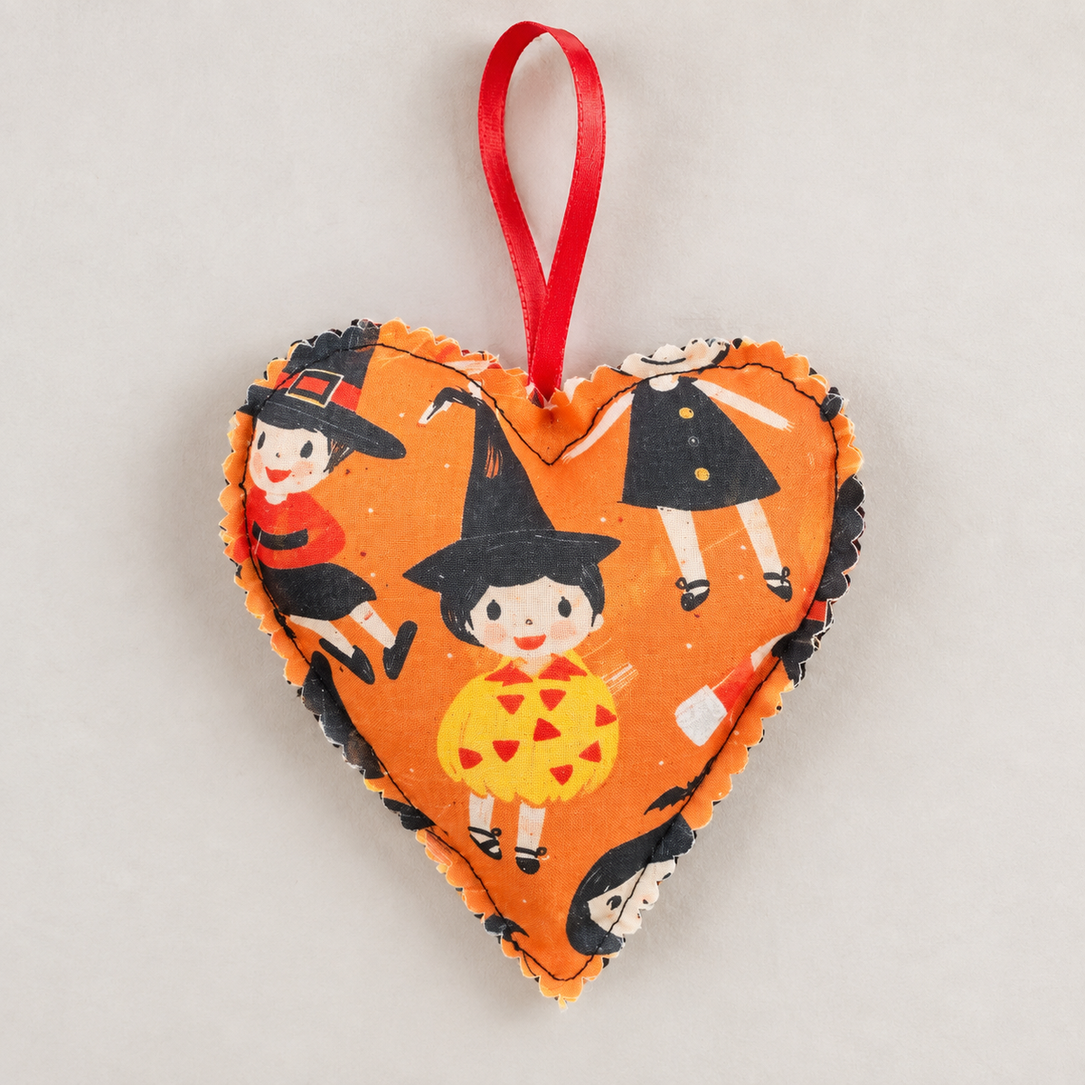 Handmade orange Halloween fabric heart hanging decoration with witches, pumpkins and bats, finished with a red ribbon loop