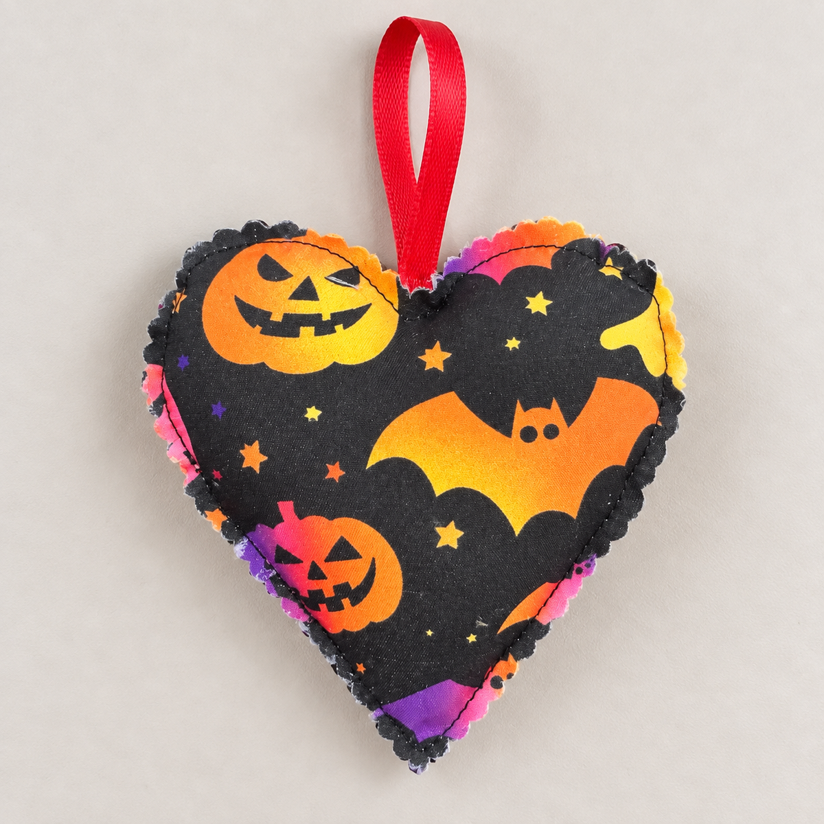 Front of handmade Halloween fabric heart decoration featuring a colourful ghost, bats and stars, with a red hanging loop
