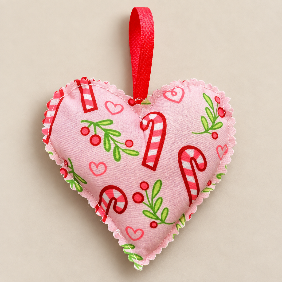 Handmade pink fabric Christmas heart with candy canes, green leaves, red berries and a red hanging ribbon