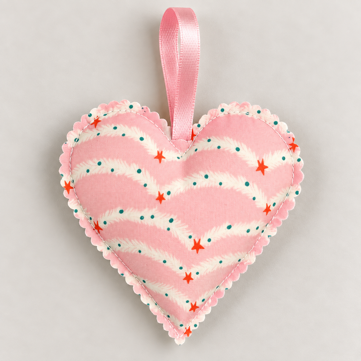 Handmade pink and cream Christmas fabric heart decorated with strings of colourful festive lights and red stars, with a pink hanging ribbon