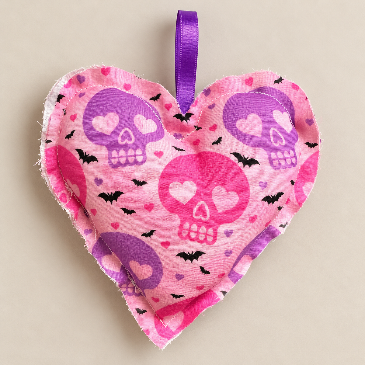 Handmade pink fabric Halloween heart with purple and pink skulls, black bats and small hearts, with a purple ribbon loop for hanging.