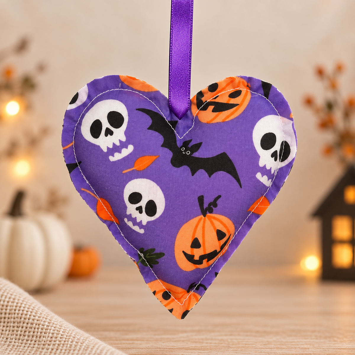 Handmade purple fabric Halloween heart ornament decorated with bats, skulls and pumpkins, finished with a purple satin hanging ribbon.