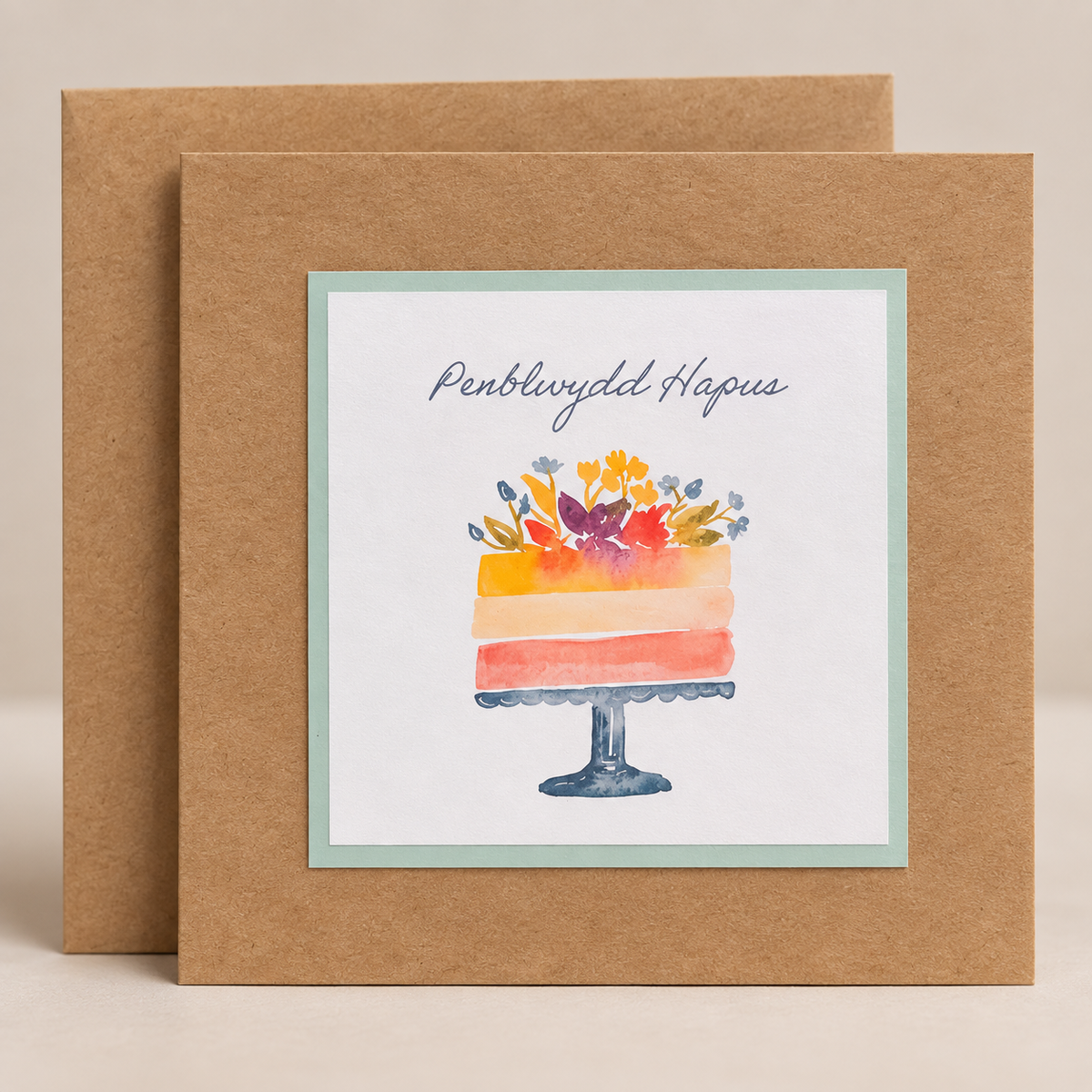 15 x 15 cm natural Kraft Welsh birthday card featuring a colourful watercolour floral cake and Penblwydd Hapus lettering, with a Kraft envelope
