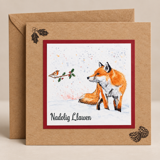 15 x 15 cm natural Kraft Welsh Christmas card featuring a watercolour fox and robin in a snowy winter scene with holly and the words Nadolig Llawen